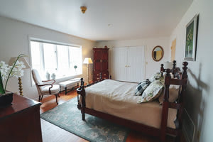 A cozy bedroom with a large bed, wooden furniture, and natural lighting from a big window.