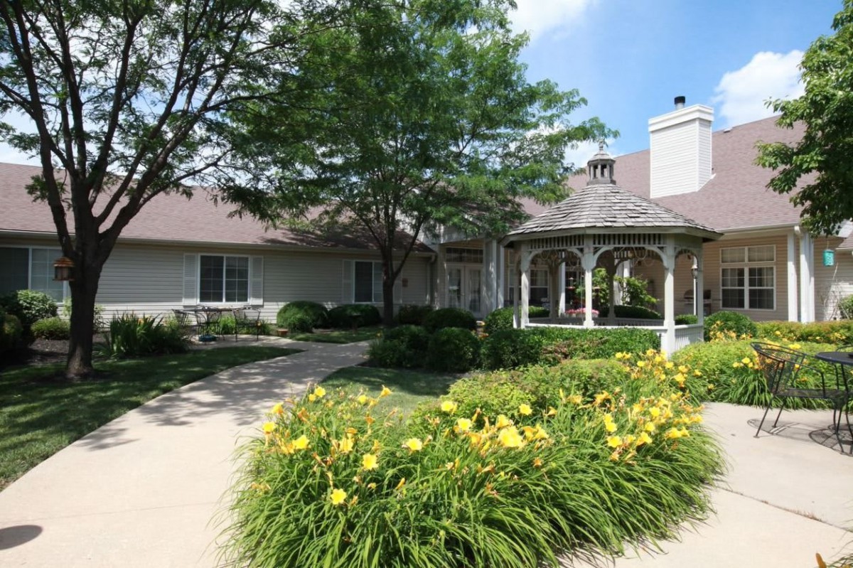 A charming house with a well-maintained garden featuring a gazebo and colorful flowers along the driveway.