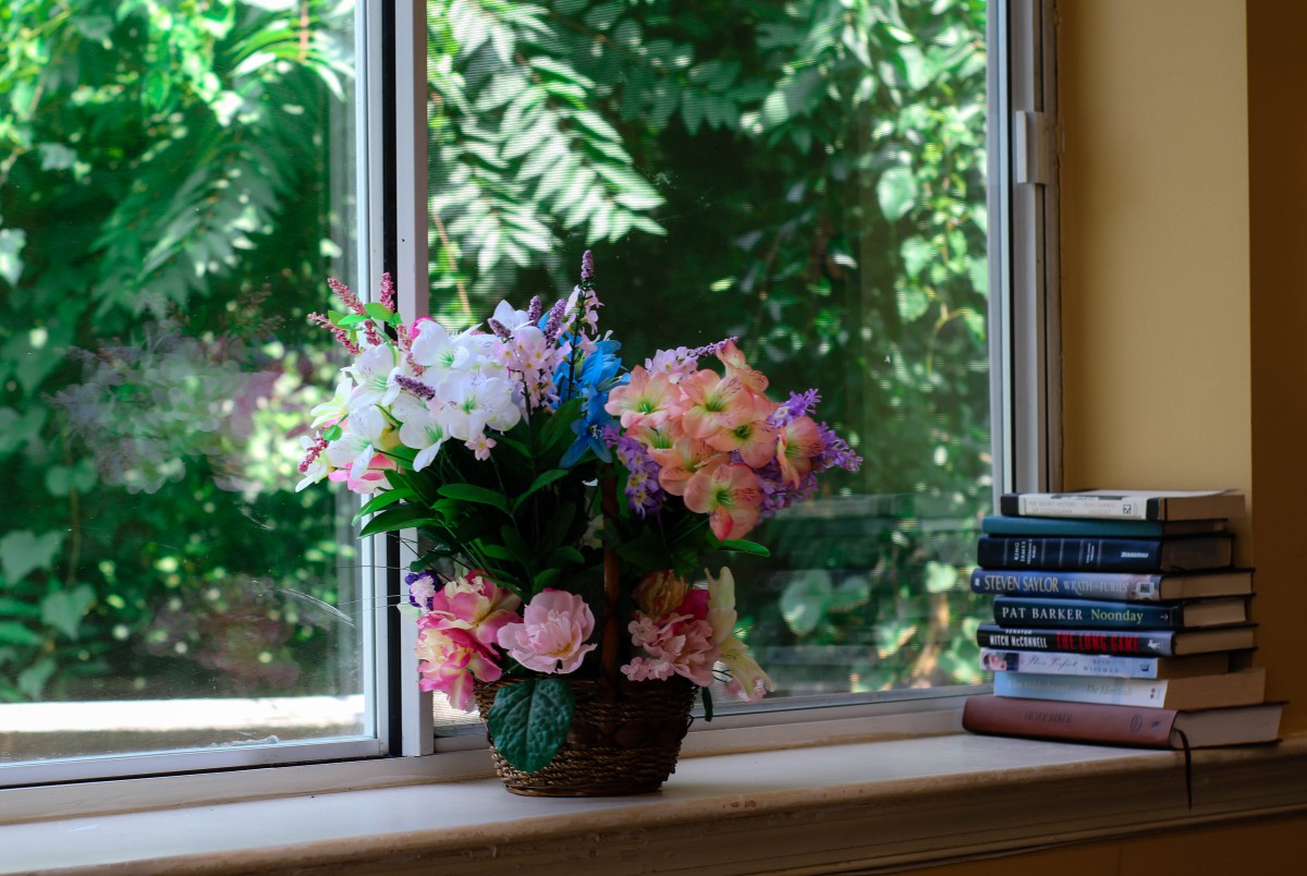 A bouquet of colorful flowers placed next to stacked books on a windowsill.