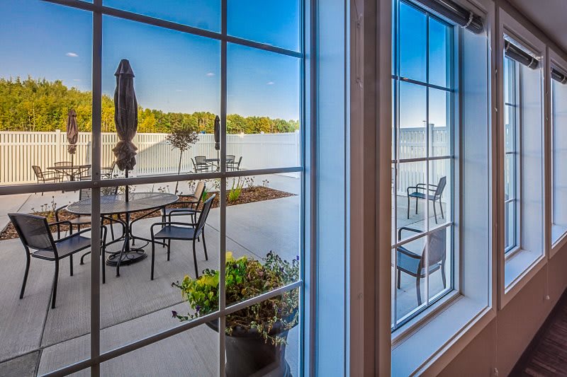 A scenic view of a patio overlooking a peaceful lake, as seen through a large window.