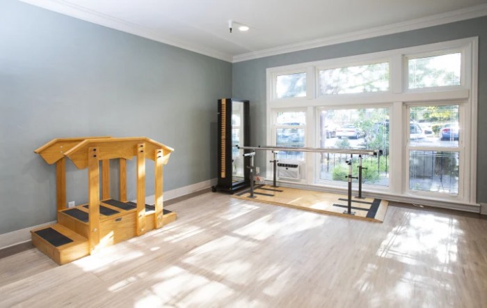 A well-lit home gym featuring a barre, mirrors, and light wood flooring.