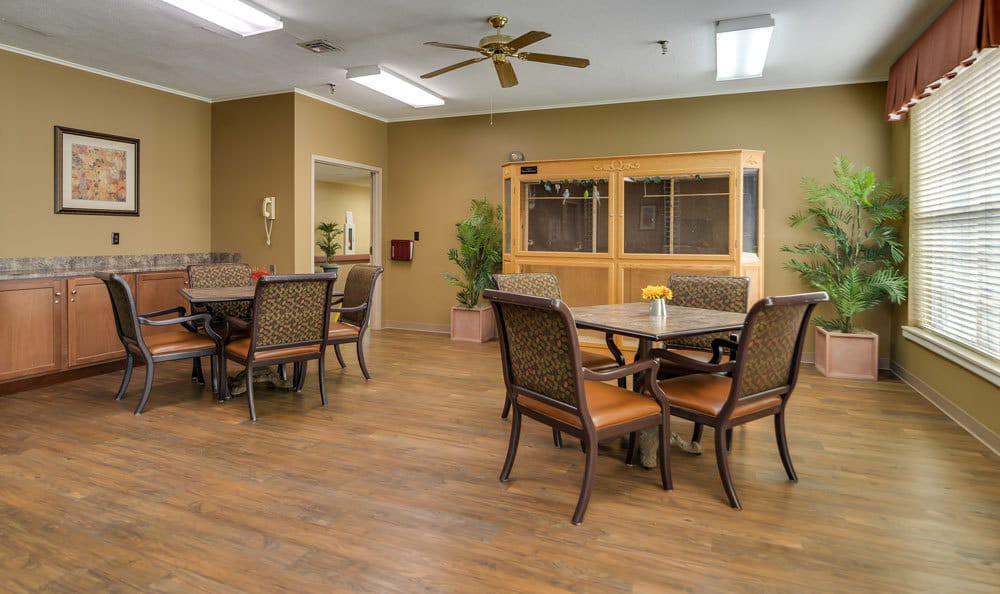 A neatly arranged dining area with multiple tables and chairs, featuring a ceiling fan and warm lighting.