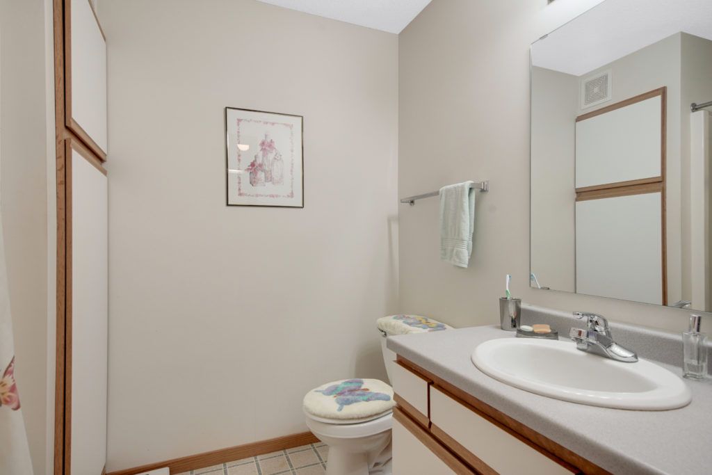 A clean and simple bathroom with a sink, toilet, mirror, and wall artwork.