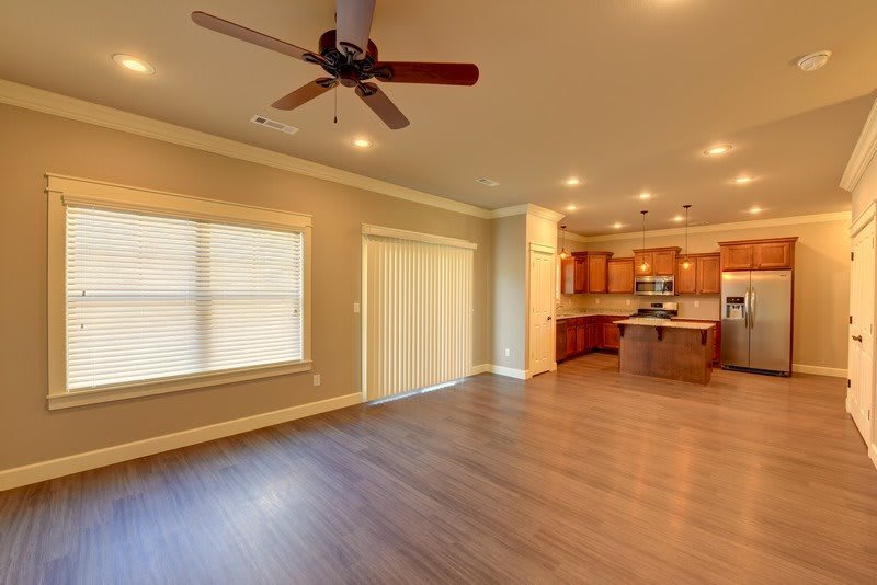 A spacious open floor plan living room leading into a kitchen with hardwood flooring and modern amenities.