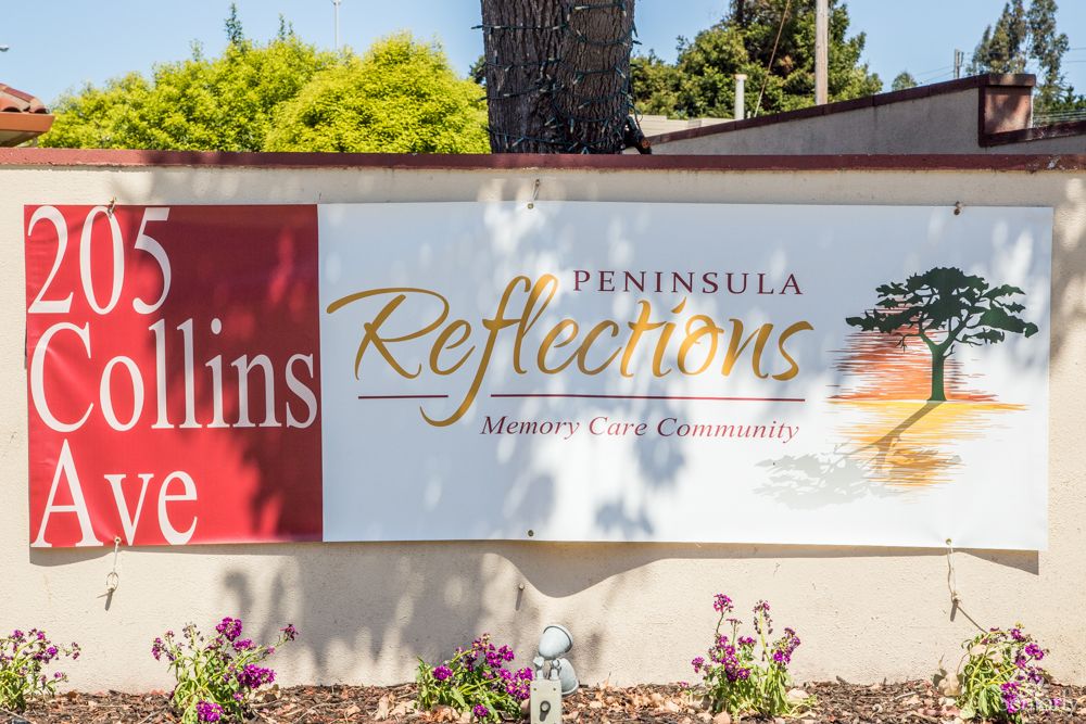Sign for Peninsula Reflections, a senior living community, surrounded by a garden.