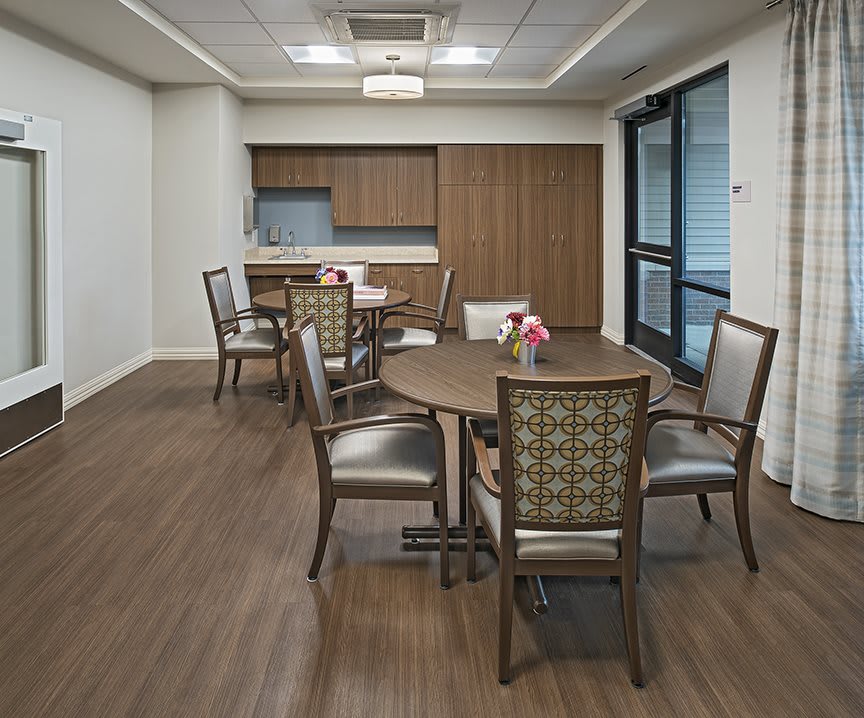 A modern dining room with a wooden floor, featuring tables and chairs, adjacent to a kitchen area.