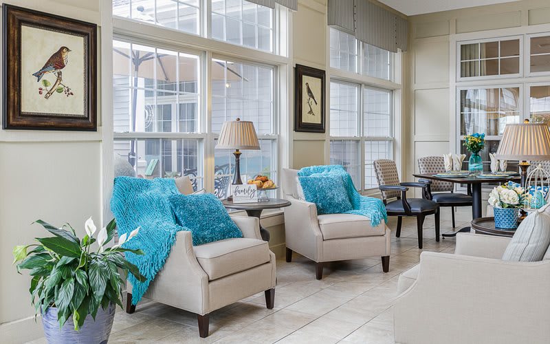 A cozy living room with armchairs and blue throws by large windows.