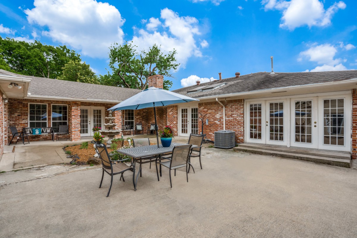 A spacious backyard patio featuring outdoor furniture and an umbrella, set against a brick house under a clear blue sky.