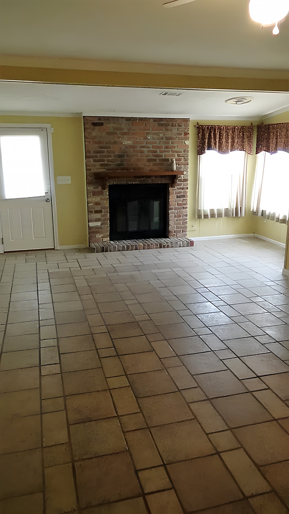 An empty living room with a brick fireplace and tile flooring.