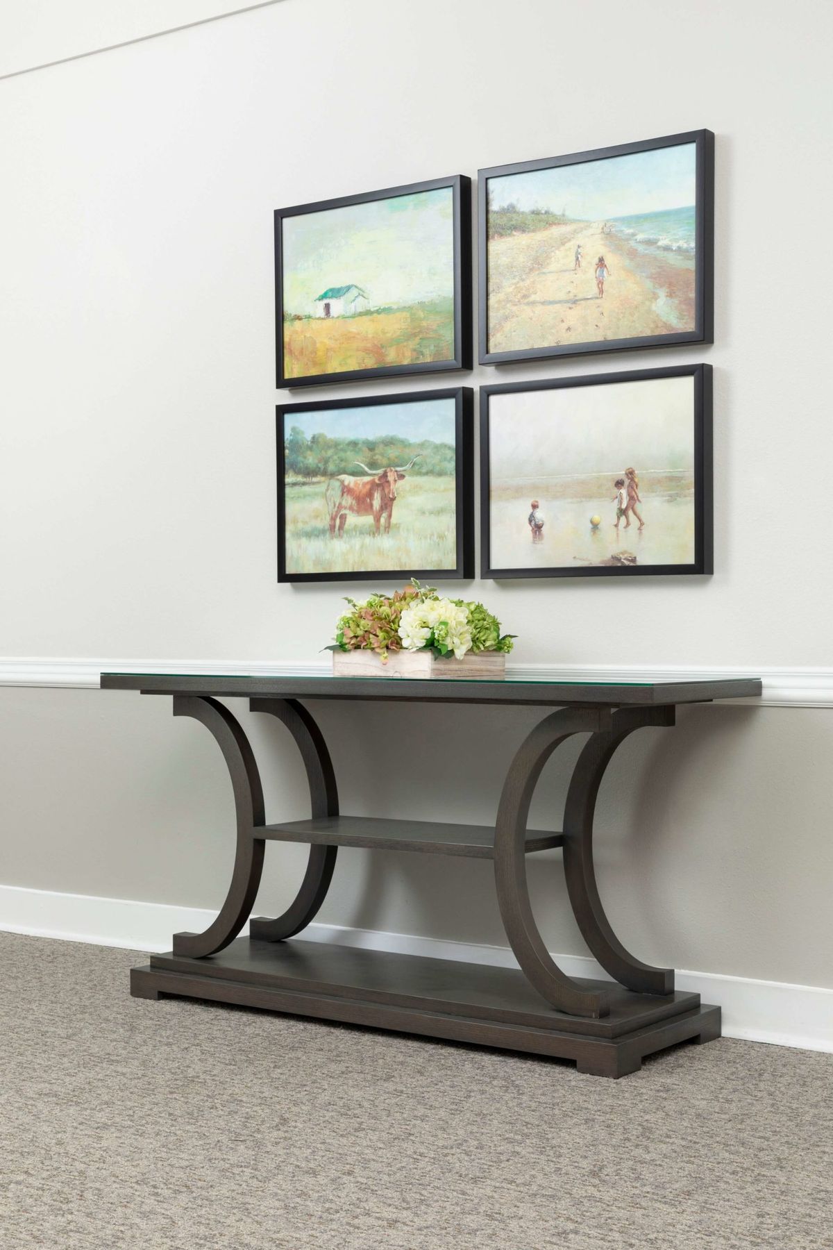 A modern console table with curved legs is adorned with a small floral arrangement, set against a wall featuring four landscape paintings.