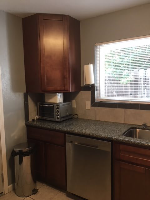 A kitchen corner with wooden cabinets, a toaster oven, and a window above the sink.