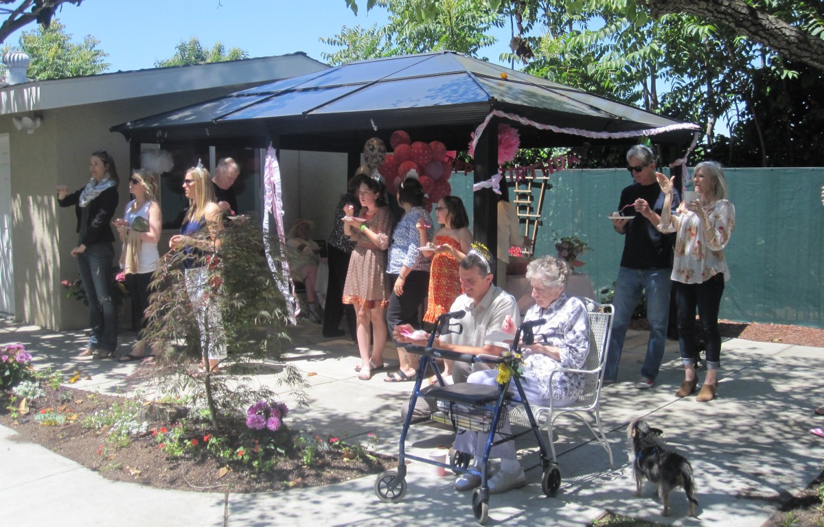 A group of people enjoy a sunny outdoor gathering in a garden setting.