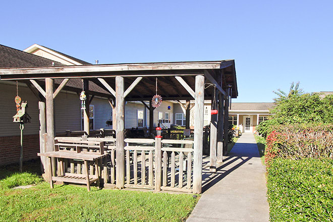 A sunlit patio with wooden structures and furniture leads to a building.
