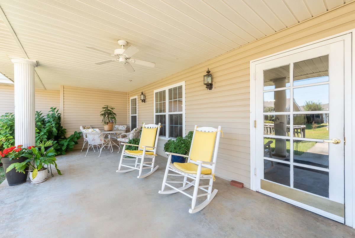 A cozy porch with rocking chairs and a table, surrounded by plants and featuring a ceiling fan.