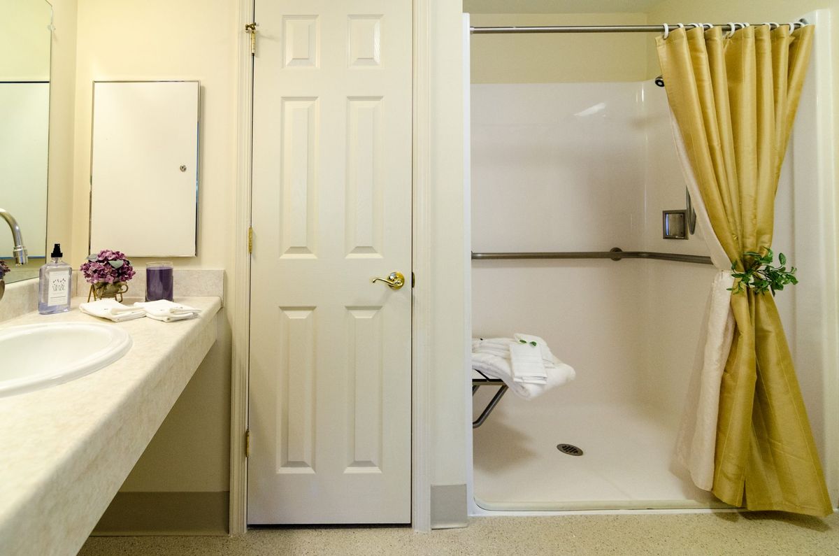 An accessible bathroom with a walk-in shower featuring grab bars and a foldable seat.
