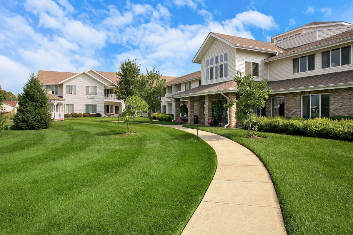 A residential building with a well-maintained lawn and a winding pathway under a blue sky.
