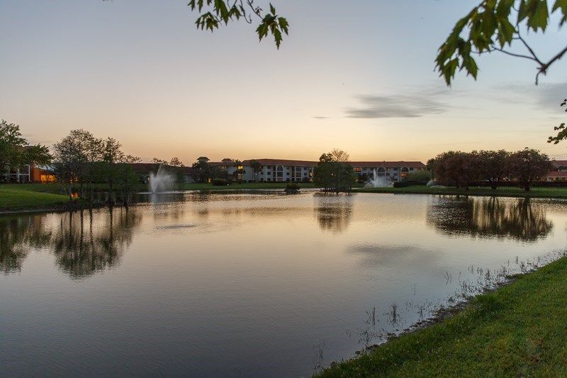 A tranquil lakeside view at sunset with calm waters reflecting the colorful sky and nearby residential buildings.