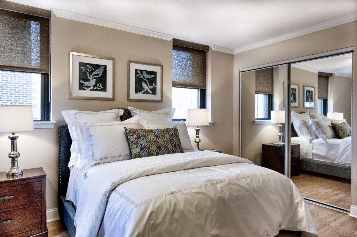 A cozy and elegantly designed bedroom with a neatly made bed, artwork on the walls, and mirrored closet doors.