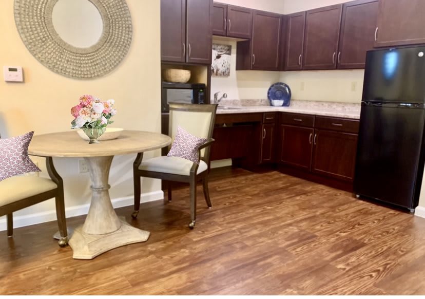 A cozy kitchen with wooden flooring, featuring dark cabinets and a small dining area with a table and chair.