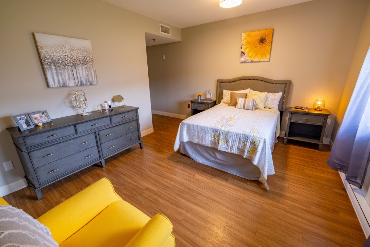 A cozy bedroom with a bed, gray dresser, and a bright yellow chair.
