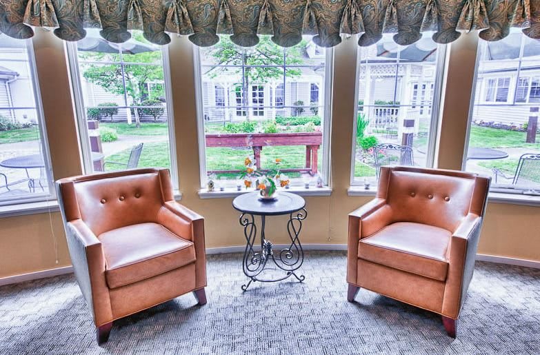 A cozy seating area with two leather chairs and a small table by the window, overlooking a garden.