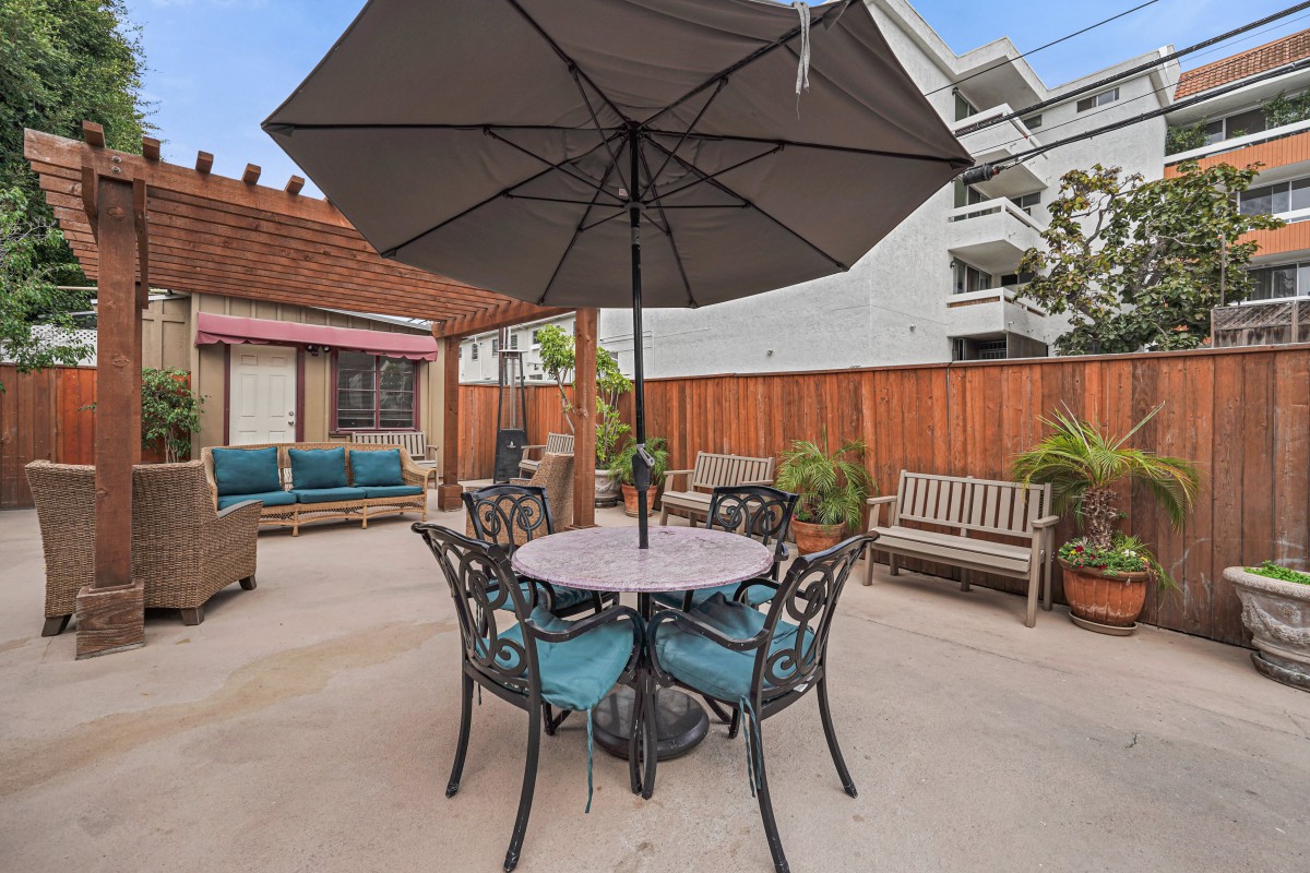 A cozy outdoor patio features a table with an umbrella, surrounded by comfortable seating and greenery.