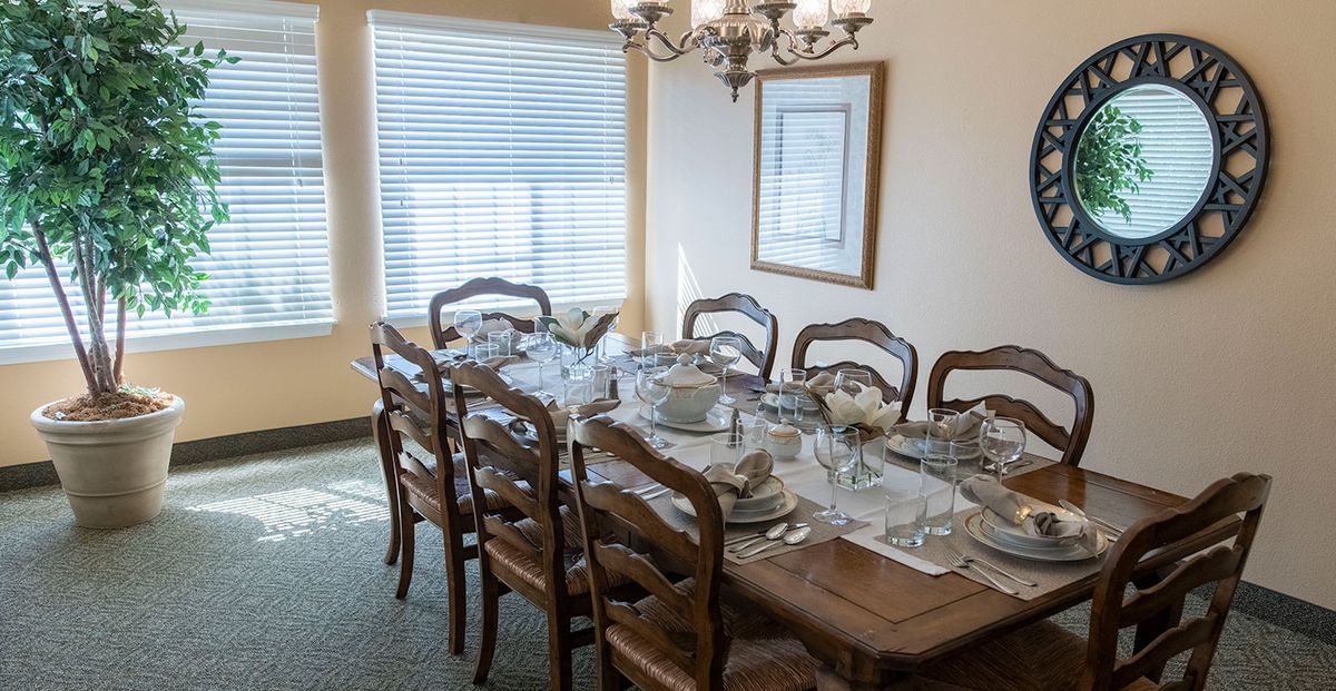 A formal dining room set up with a table prepared for a meal, featuring elegant tableware and a chandelier above.