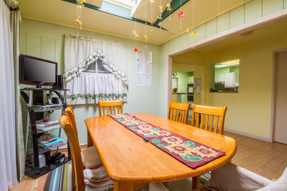 A cozy dining room with a wooden table, chairs, and a colorful table runner under a skylight.