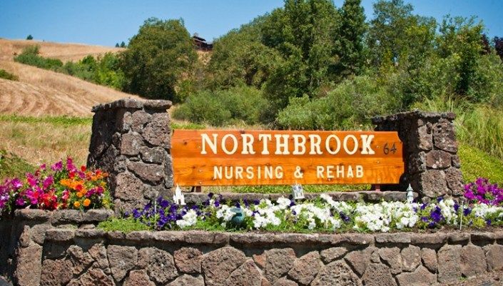 Sign for Northbrook Nursing & Rehab surrounded by greenery and flowers.