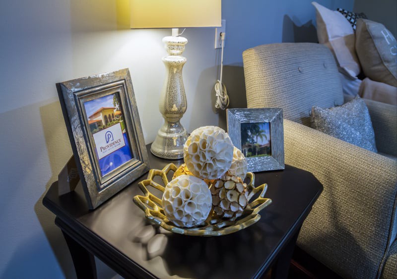 A cozy living room table with a lamp, decorative bowl, and framed photos.