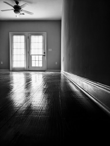 A serene view of an empty room with polished wooden floors reflecting light, leading to an inviting doorway.