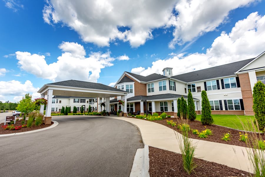 A modern residential building with a landscaped driveway under a partly cloudy sky.