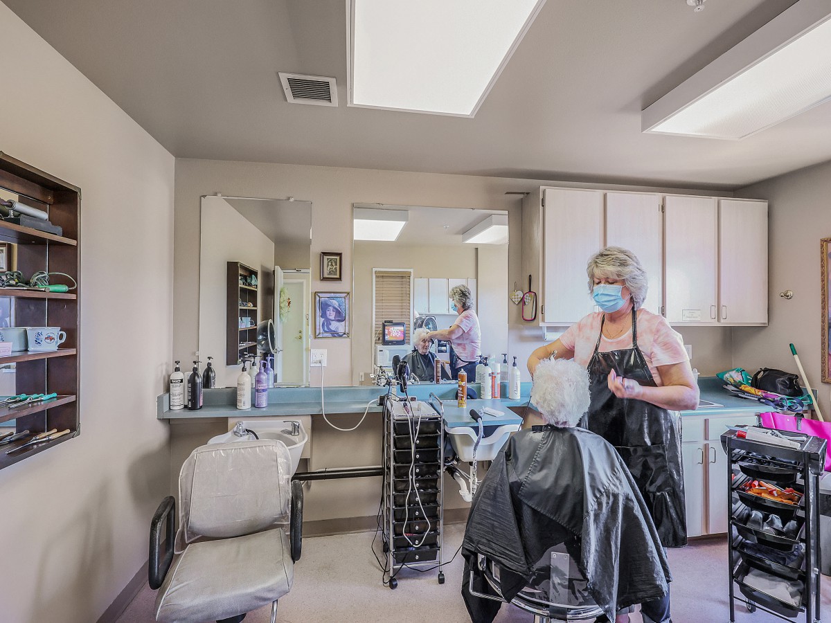 A hairdresser wearing a mask styles a client's hair in a salon.