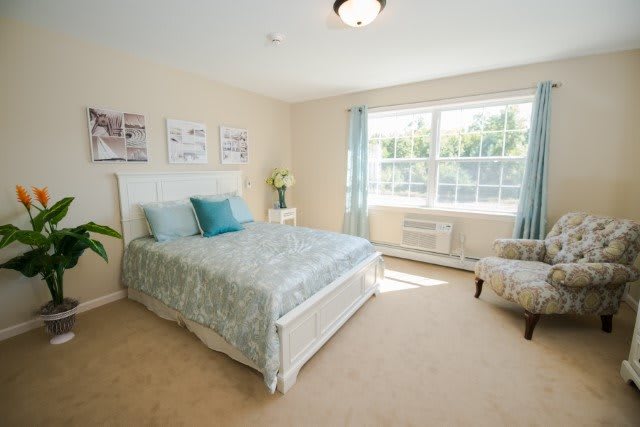 A bright and airy bedroom with a neatly made bed, large window, and tasteful decor.