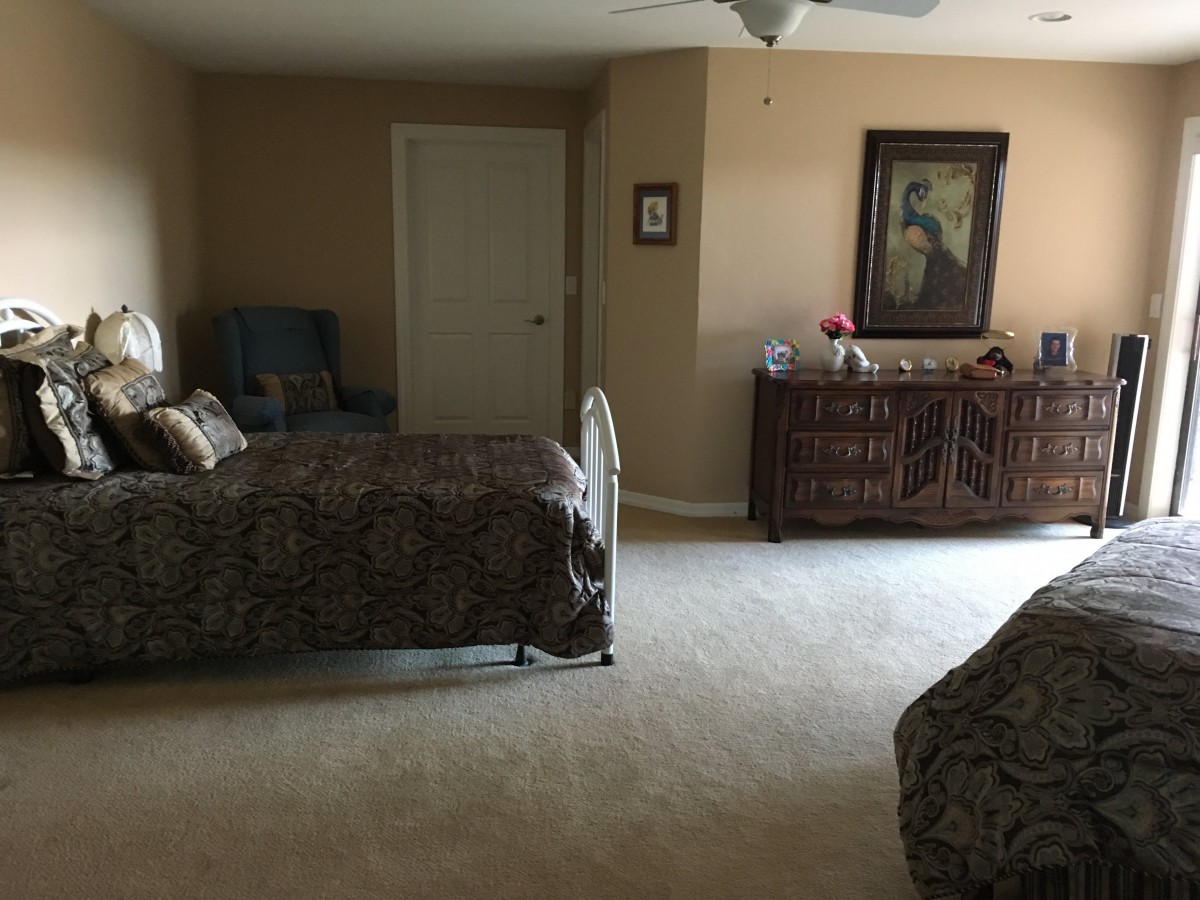 A spacious bedroom with a bed, dresser, and carpeted floor.