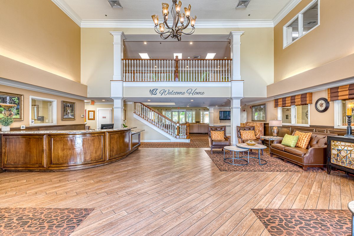 A spacious hotel lobby with a reception desk, seating area, and a grand staircase.