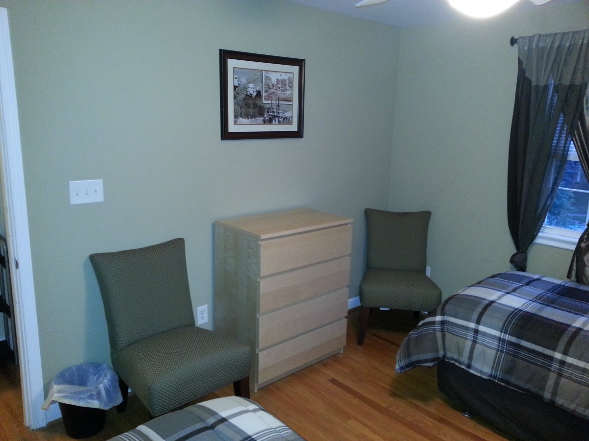 A neatly arranged bedroom with two beds, chairs, and a dresser.