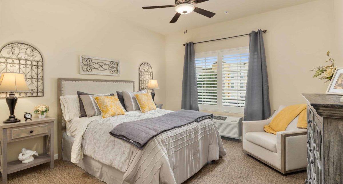 A cozy bedroom with a large bed, decorative pillows, curtains, and a ceiling fan.