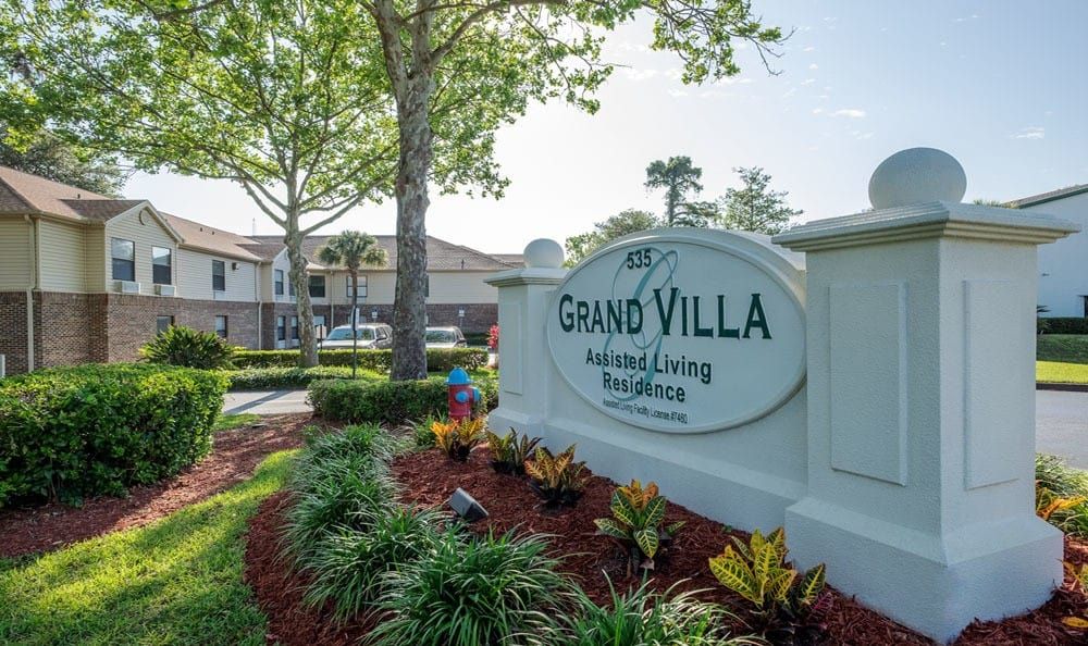 The entrance to Grand Villa Assisted Living Residence featuring well-maintained landscaping and clear signage.