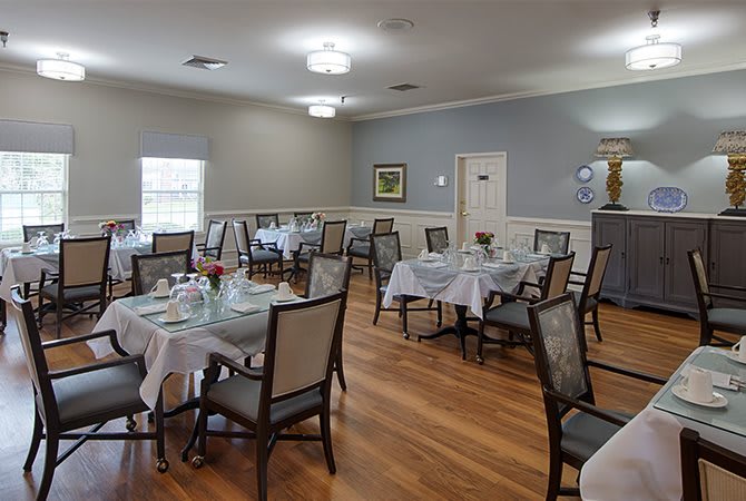 An elegantly arranged dining room with neatly set tables and chairs on a polished wooden floor.