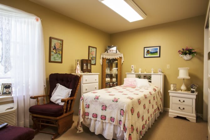 A cozy bedroom with a single bed featuring a patterned quilt, accompanied by a rocking chair and classic decor.