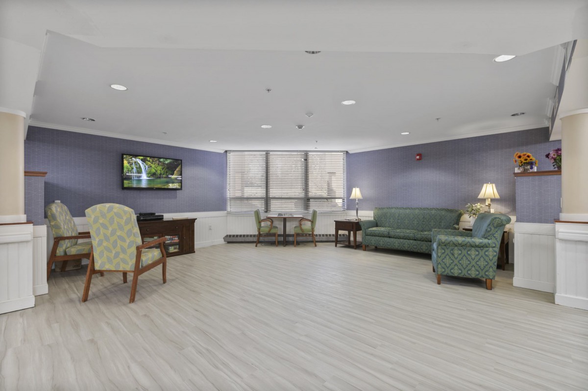 A spacious living room with a sofa, chairs, a table, and a mounted television.