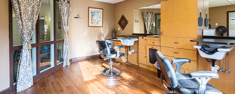 A well-lit hair salon interior with a barber chair, sink, and large mirror on a wooden floor.
