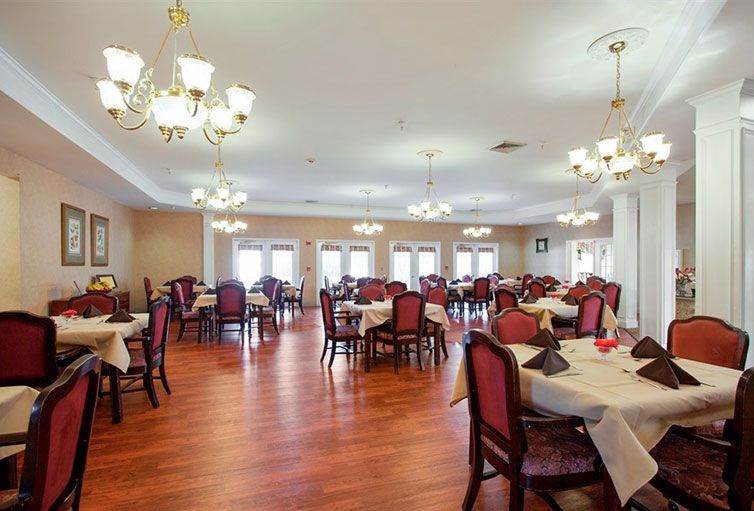 An elegant dining room with neatly arranged tables and chairs, illuminated by chandeliers.