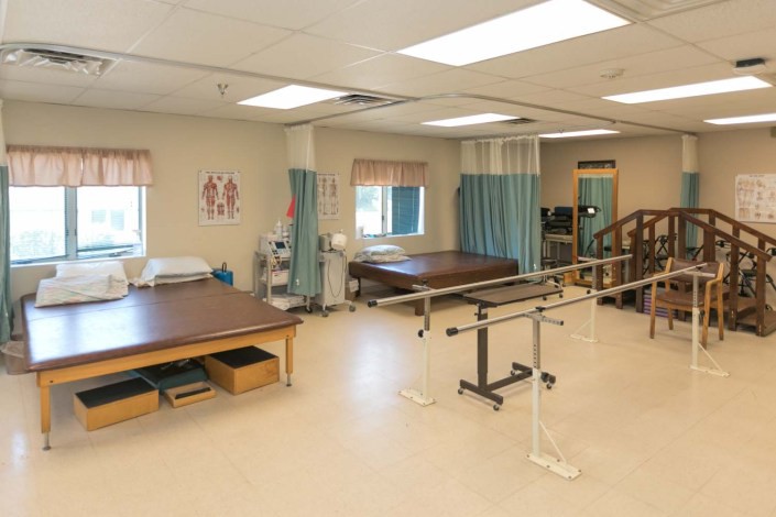 A physical therapy room equipped with therapy beds and parallel bars, designed for rehabilitation exercises.