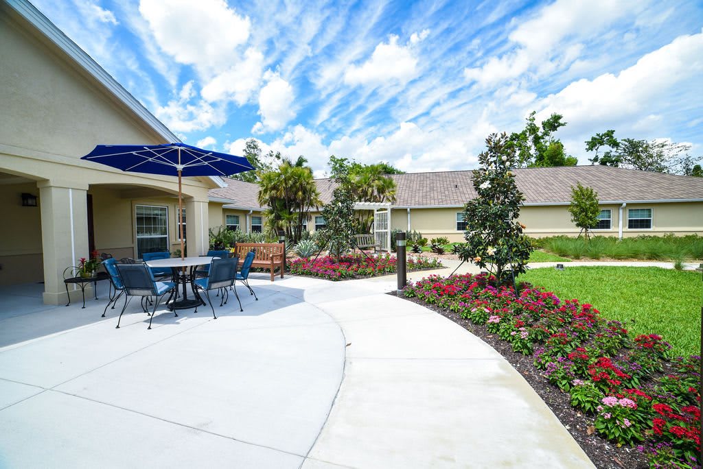 A sunny garden patio with a pathway, surrounded by vibrant flowers and outdoor seating.