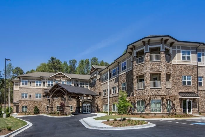 A stone-clad, three-story building with a central entrance and surrounding landscaping under a clear blue sky.