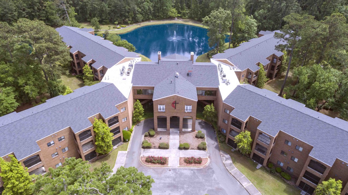 Aerial view of a residential apartment complex with a pond and surrounding greenery.