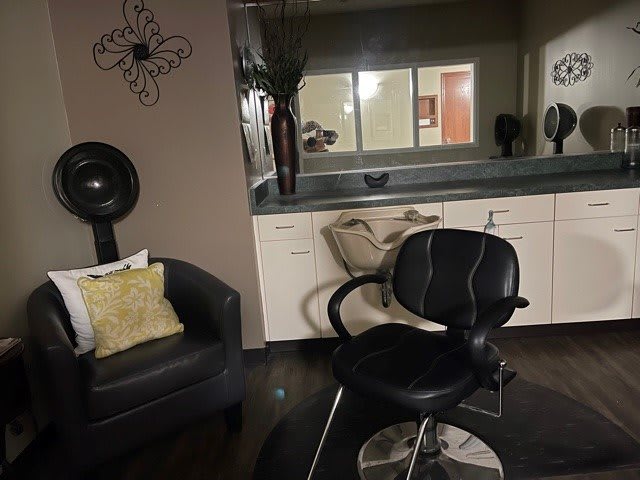 A cozy salon interior with a styling chair, mirror, and comfortable seating.