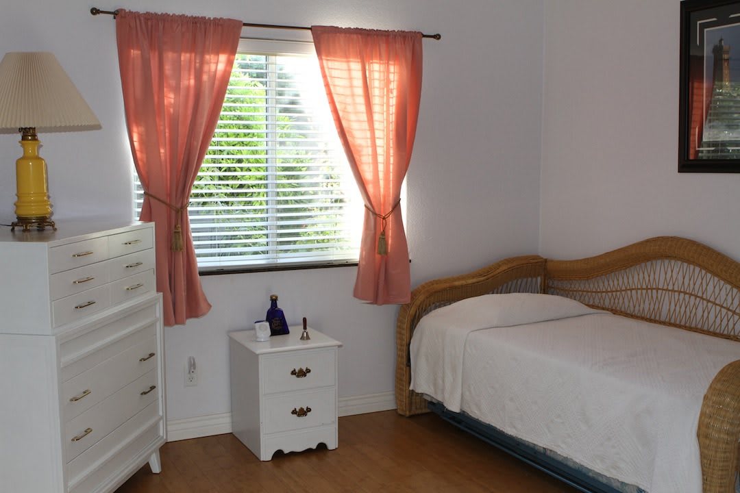 A cozy bedroom with a bed, nightstand, and dresser near a window with pink curtains.